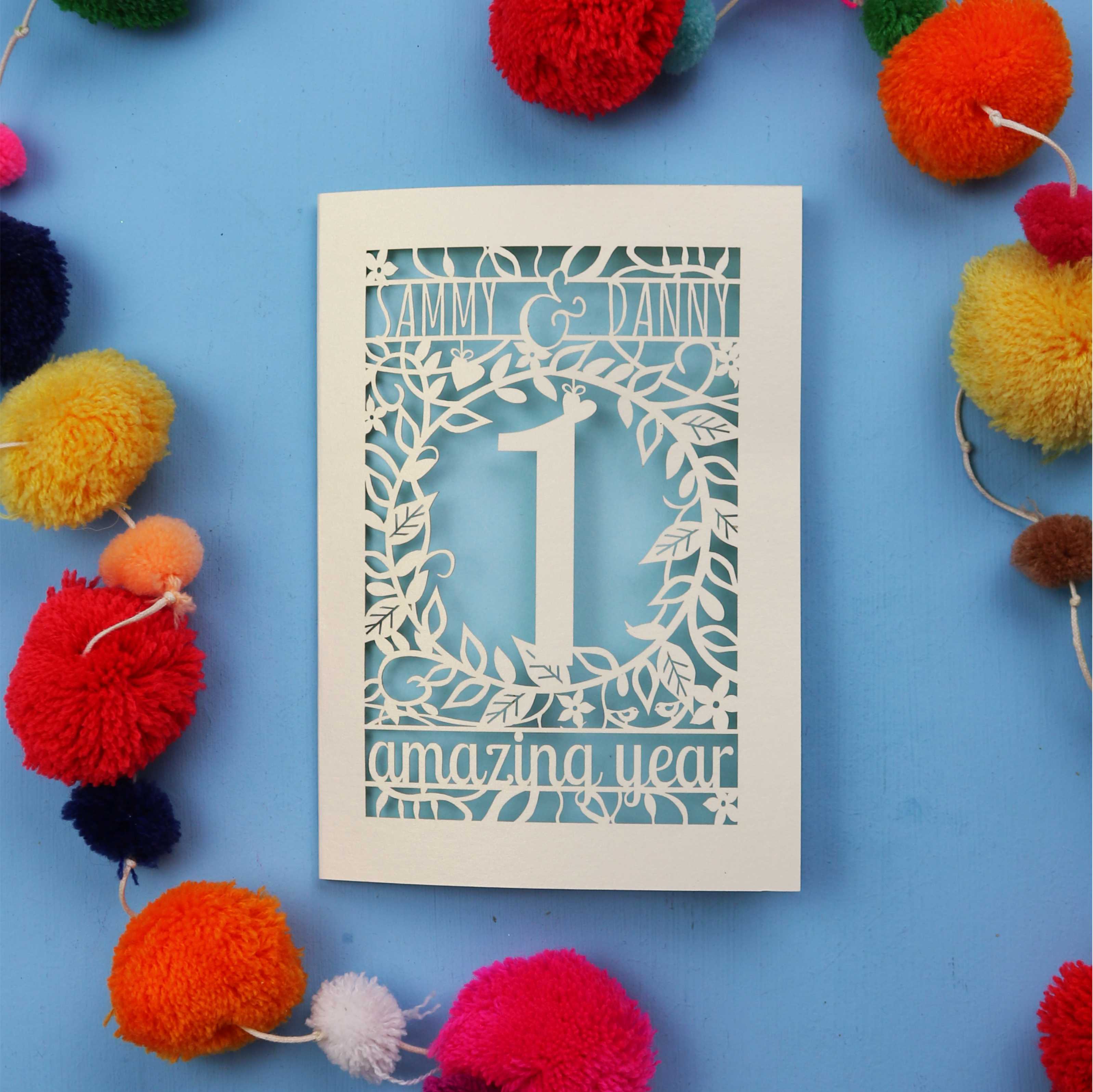 1st wedding anniversary Card with cut-out design on a blue background with colourful pom-poms