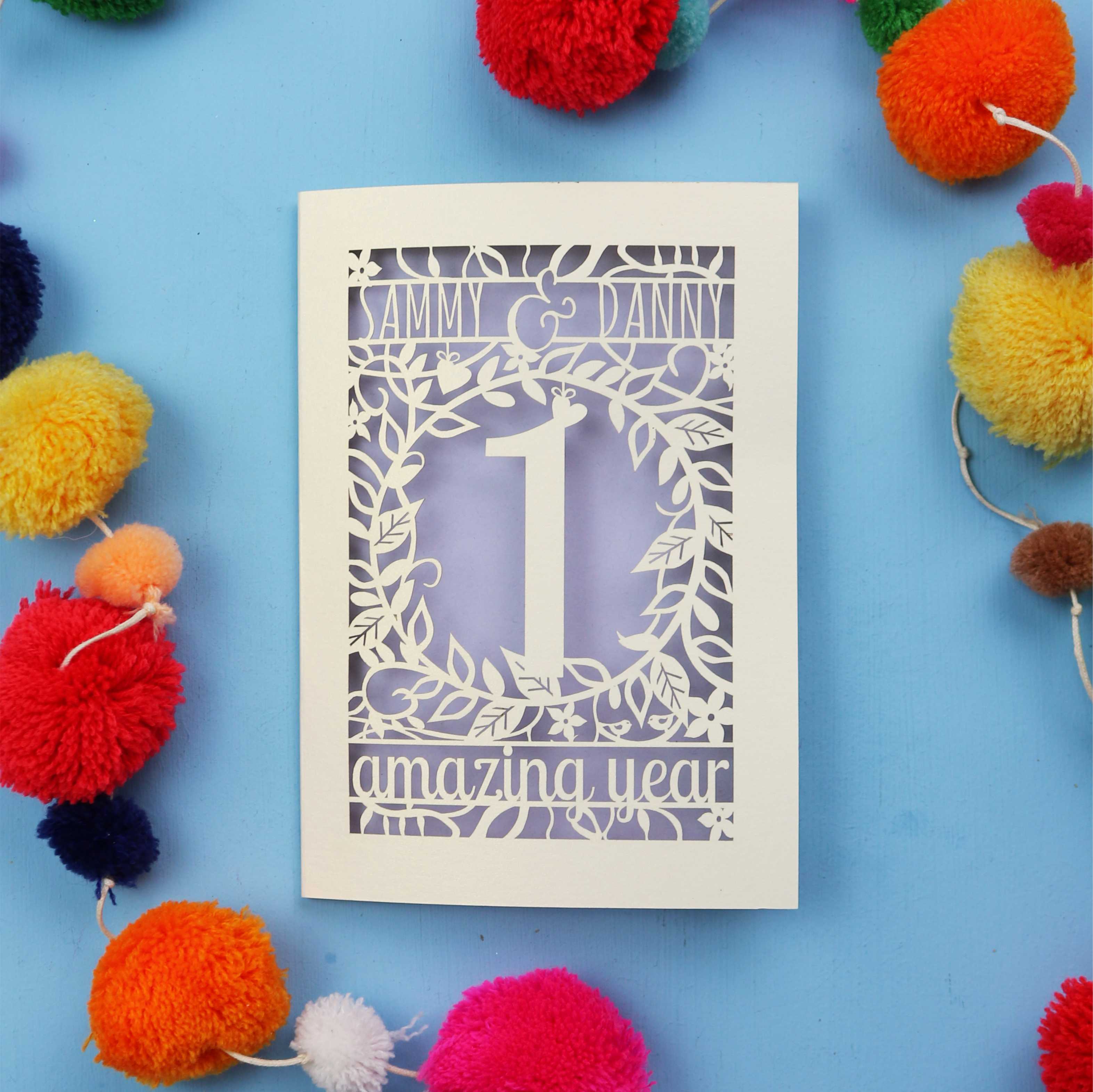 1st wedding anniversary Card with cut-out design on a blue background with colourful pom-poms