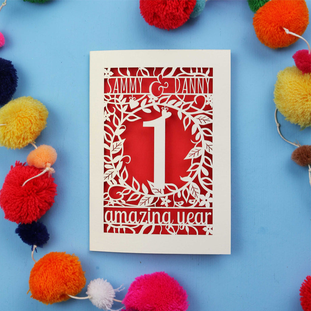 1st anniversary Card with cut-out design on a blue background with colourful pom-poms