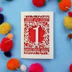 1st anniversary Card with cut-out design on a blue background with colourful pom-poms