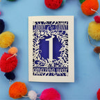 1st wedding anniversary Card with cut-out design on a blue background with colourful pom-poms
