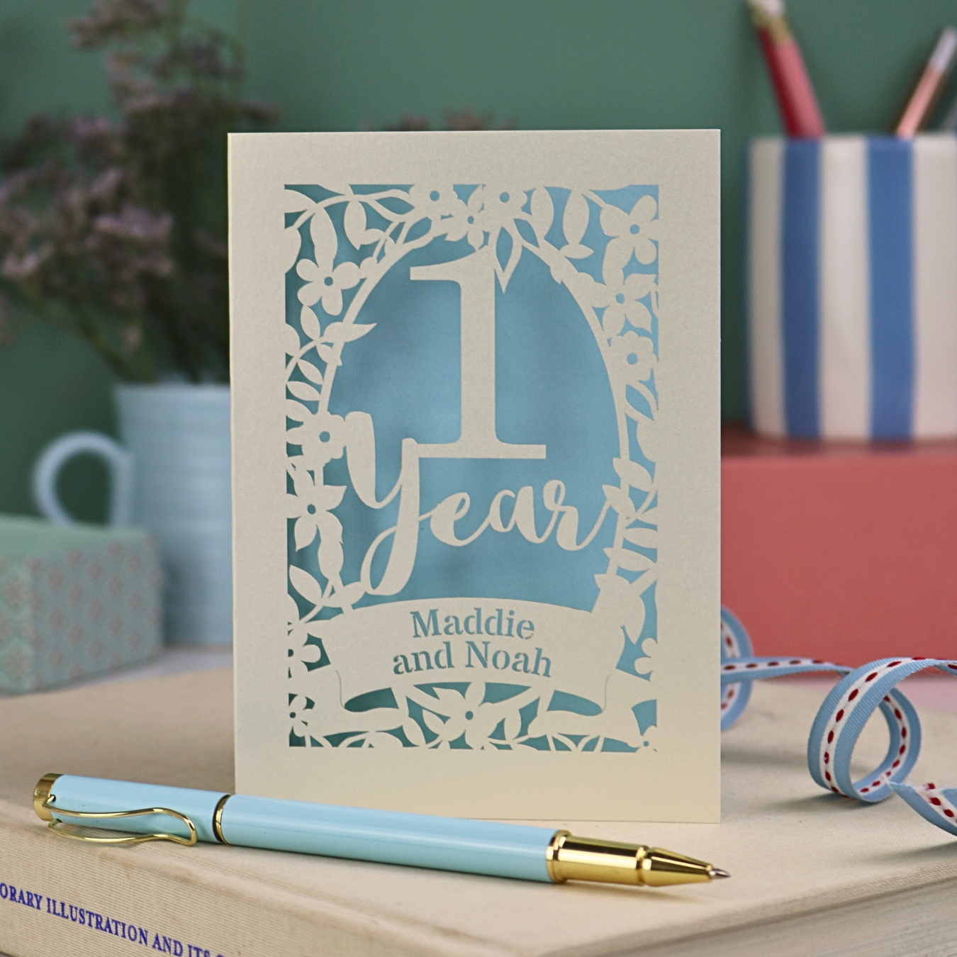 First anniversary Card with '1 Year' and 'Maddie and Noah' text on a desk with stationery items.