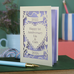 A laser cut cream first anniversary card with banners and heart design and the text "Happy 1st Anniversary Lia & Cam" with a banner above and the year 2025, and a banner below with the year 2026