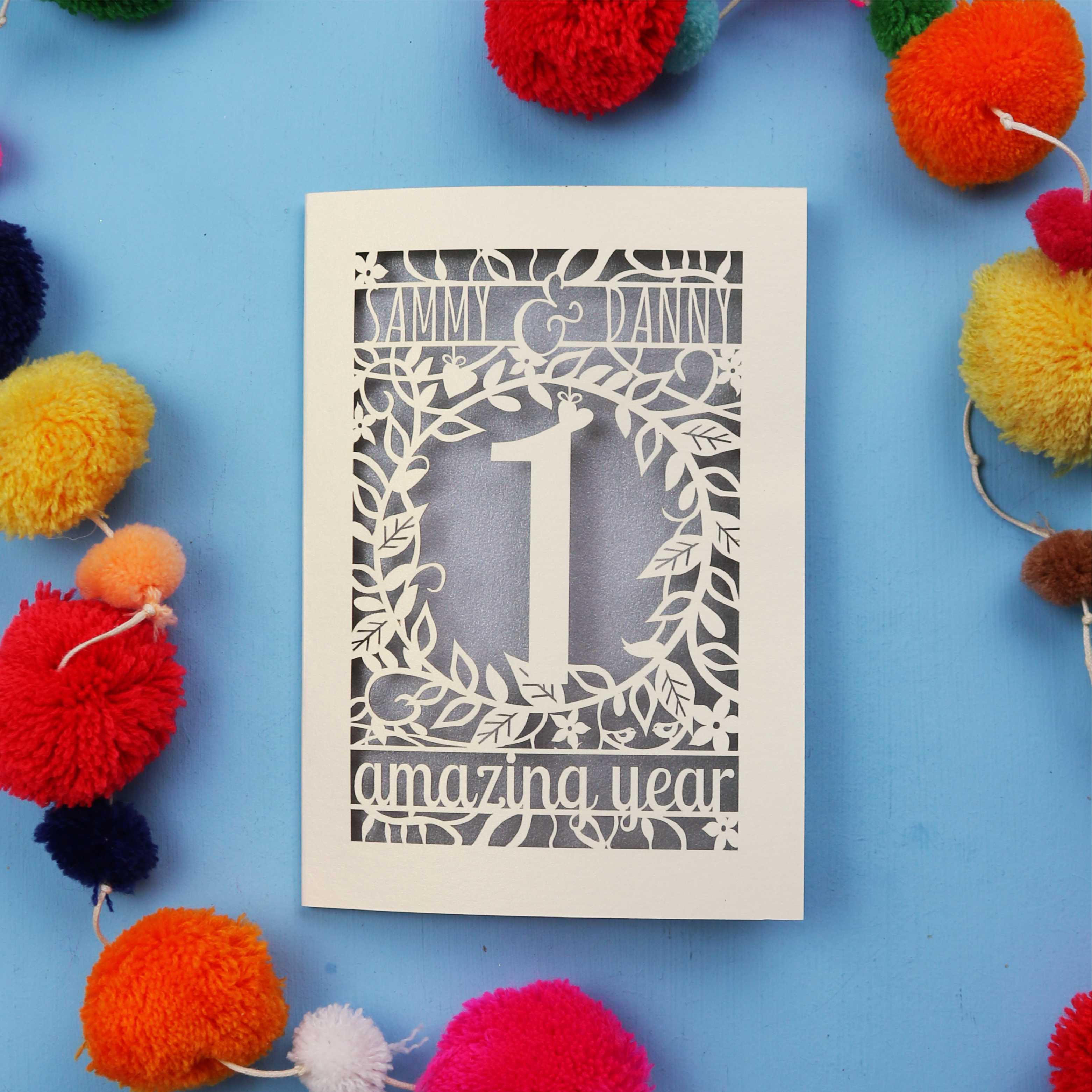 First anniversary Card with cut-out design on a blue background with colourful pom-poms