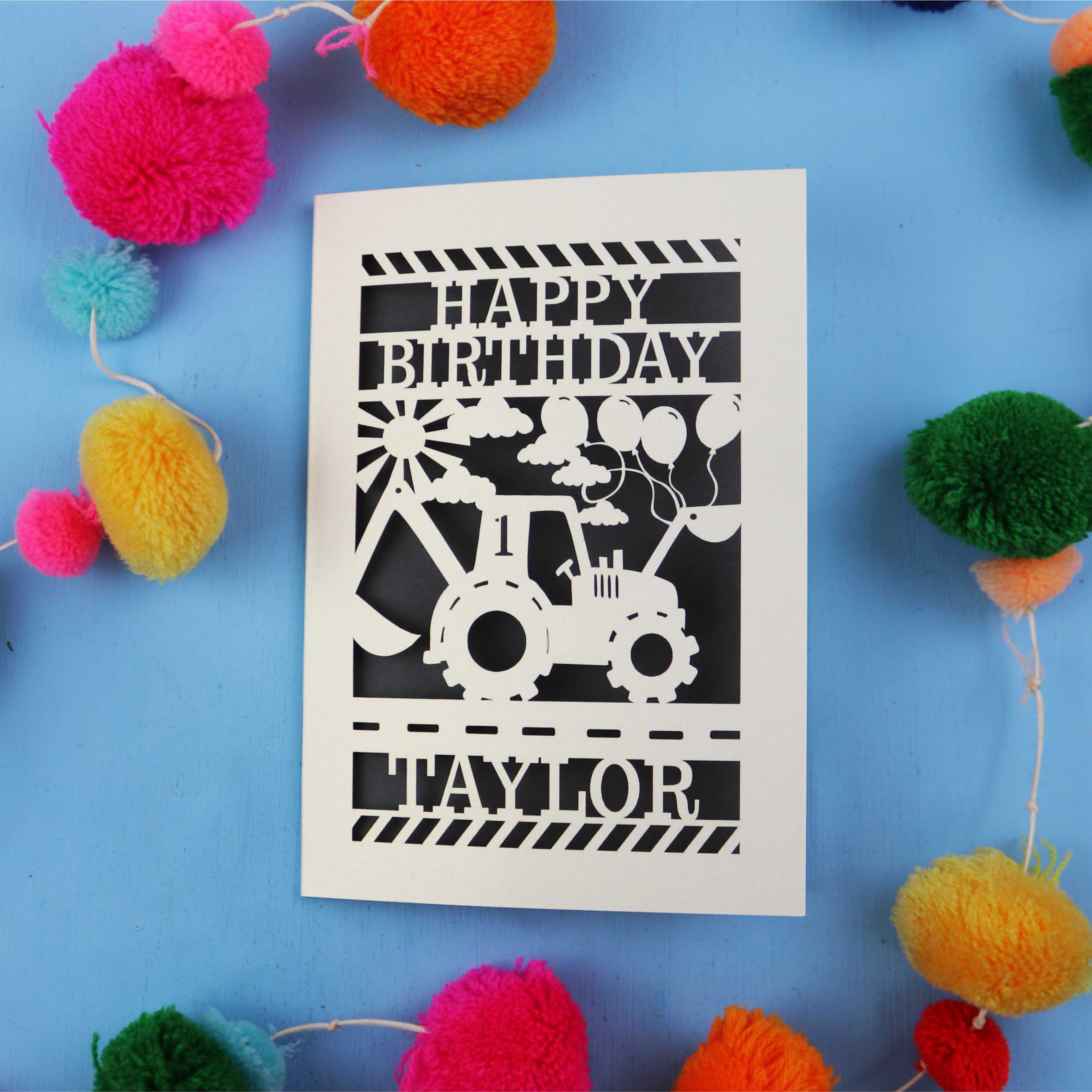 1st Birthday card with a tractor design and 'Happy Birthday Taylor' text on a blue background with colourful pom-poms.