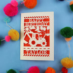 1st Birthday card with a digger design and 'Happy Birthday Taylor' text on a blue background with colourful pom-poms.