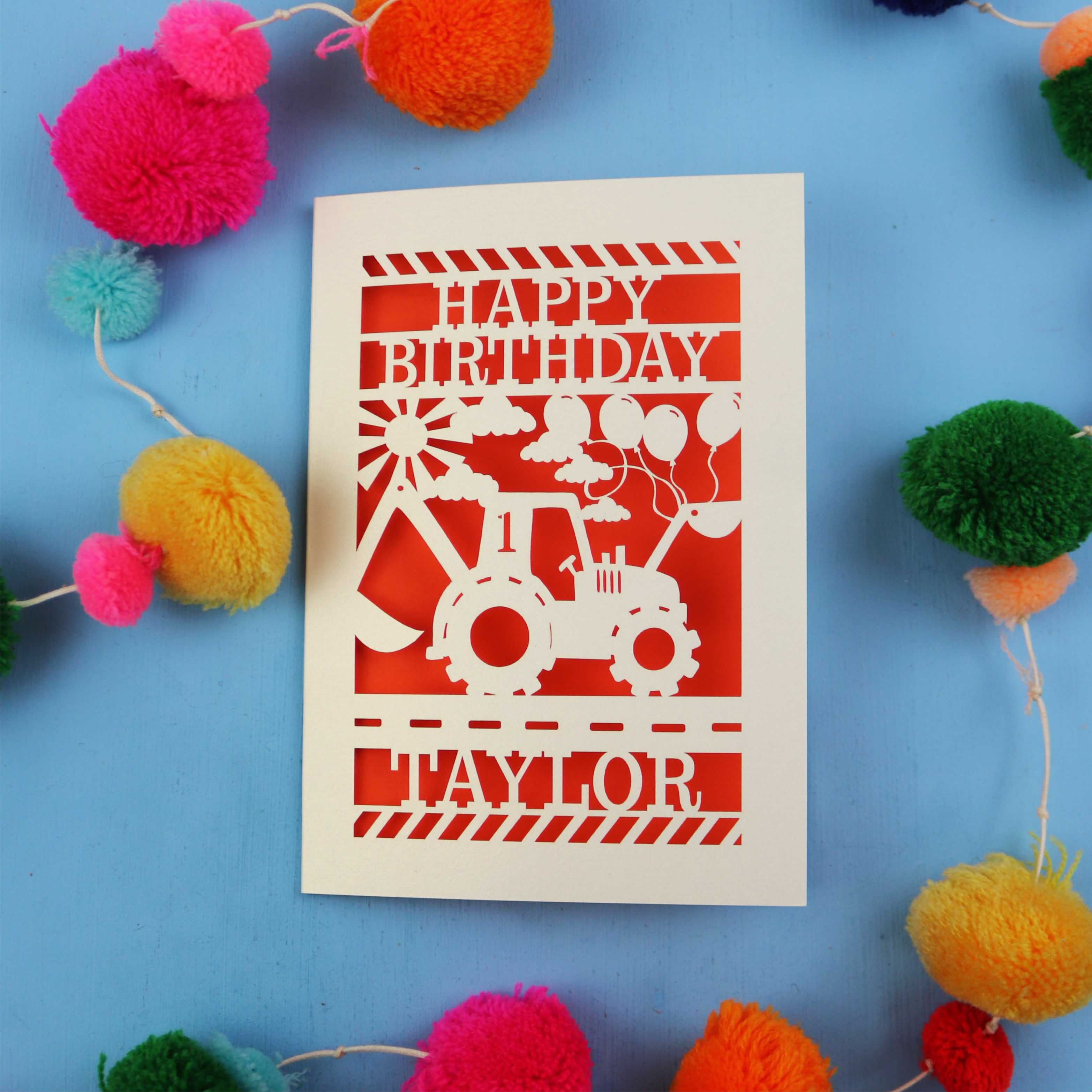 1st Birthday card with a digger design and 'Happy Birthday Taylor' text on a blue background with colourful pom-poms.