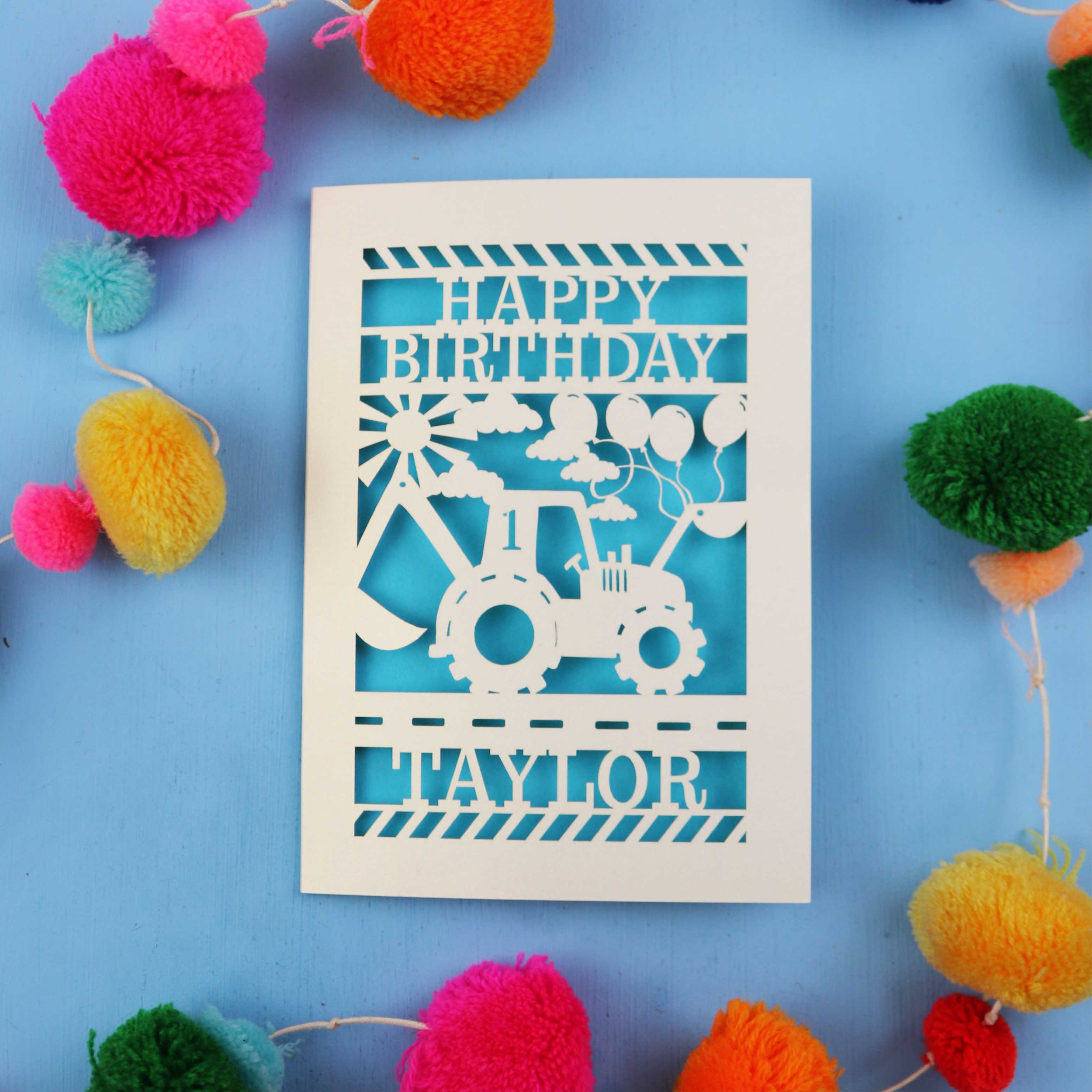 1st Birthday card with a tractor design and 'Happy Birthday Taylor' text on a blue background with colourful pom-poms.