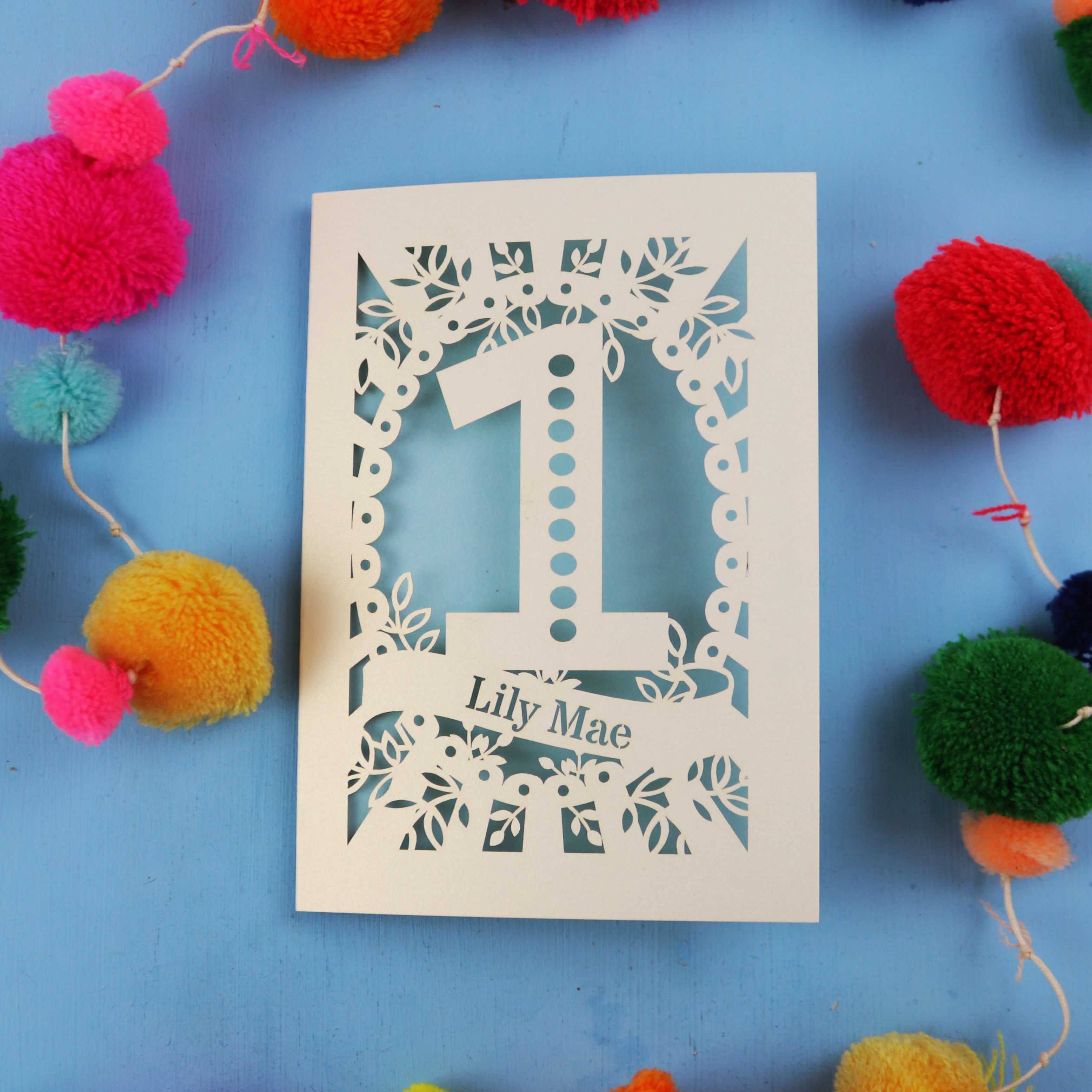 Baby's Birthday Card with '1' and 'Lily Mae' on a blue background with colourful pom-poms