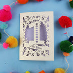 Laser-cut card with '1' and 'Lily Mae' text on a blue background with colourful pom-poms.