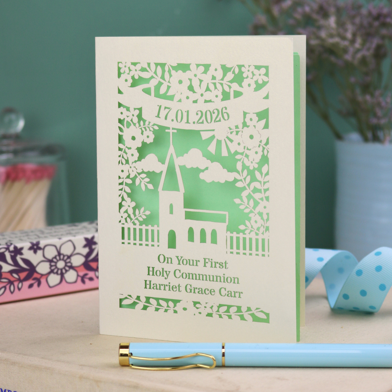 Personalized card with a church design and text on a wooden surface with a pen and decorative items.