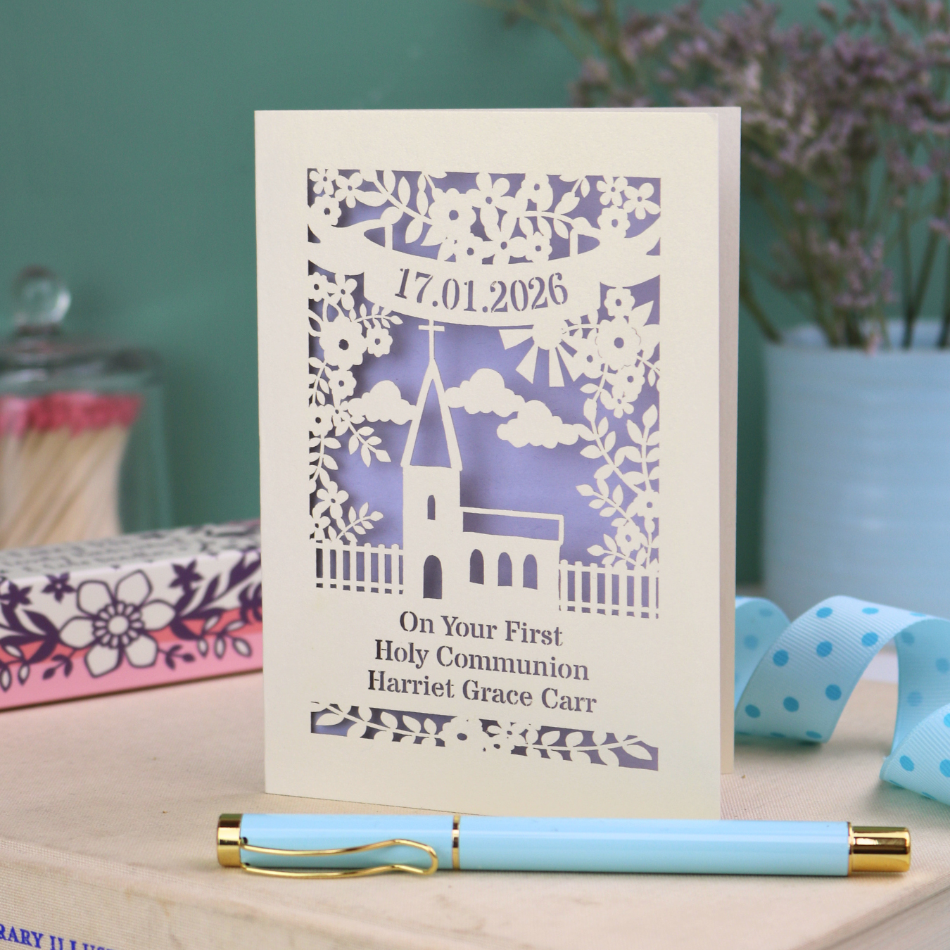 A cream laser cut 'On Your First Holy Communion' card with cut out church design, floral border, the date and name in cut out stencil font.