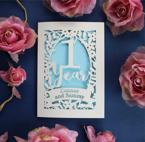 A papercut card for a first anniversary. Personalised cards contain the names of the couple in a banner.  - A5 (large); / Light Blue