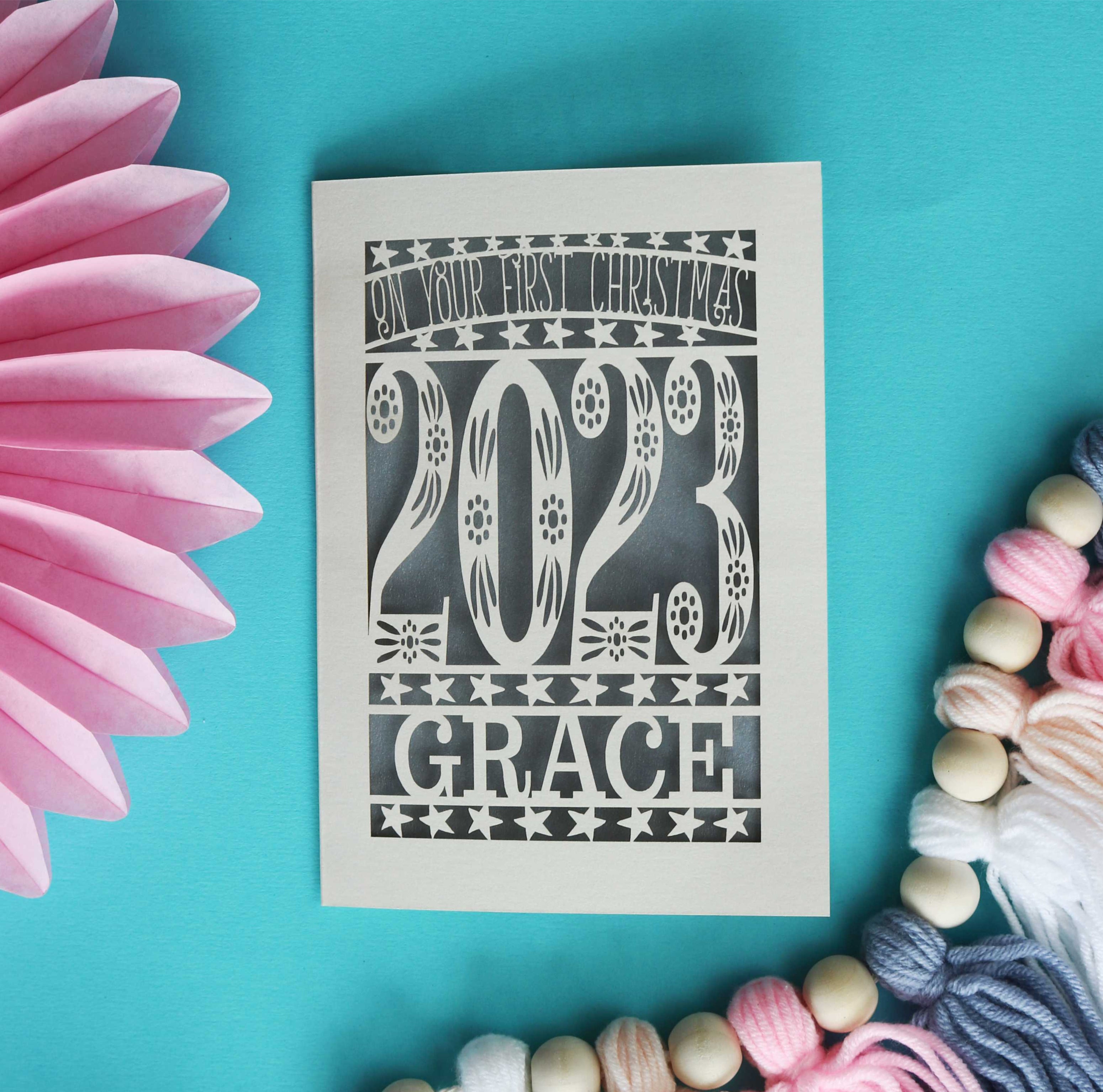 A papercut card in cream with a grey insert to celebrate a baby's first Christmas. Shows the current year and baby's name.