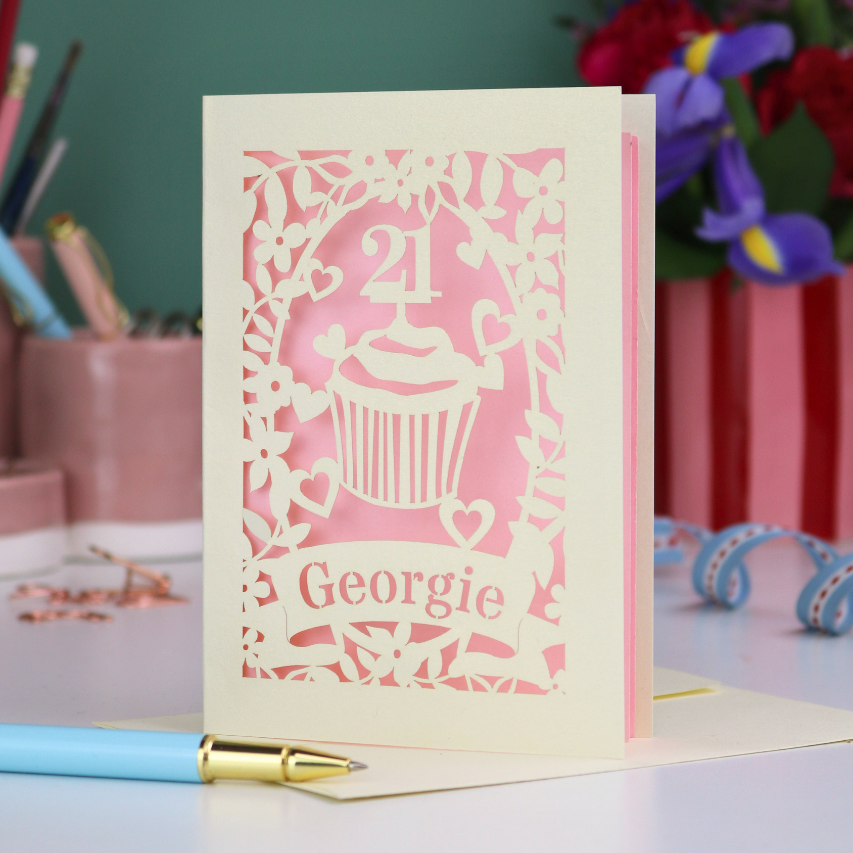 Laser-cut 21st birthday card with personalised cupcake design and 'Georgie' text on a desk with stationery items.