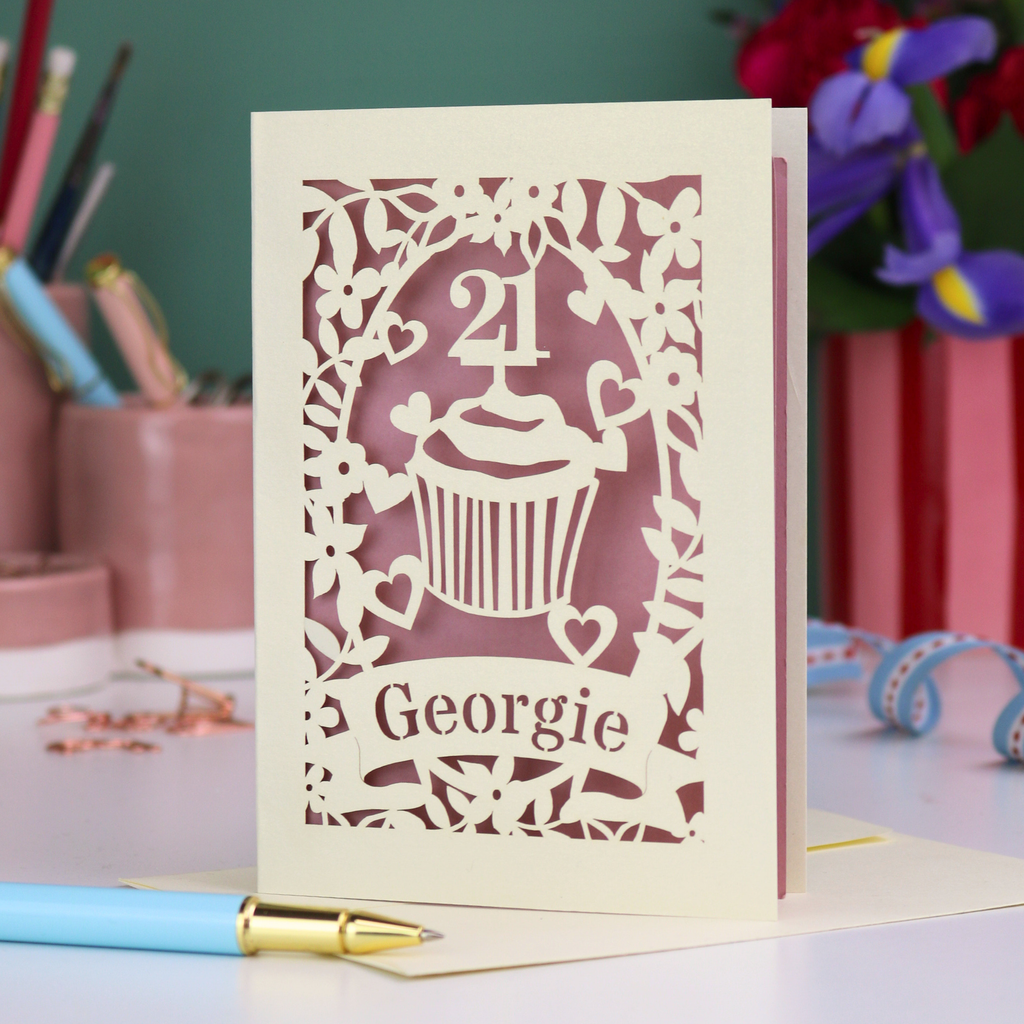 Laser-cut 21st birthday card with personalised cupcake design and 'Georgie' text on a desk with stationery items.