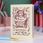 Laser-cut 21st birthday card with personalised cupcake design and 'Georgie' text on a desk with stationery items.
