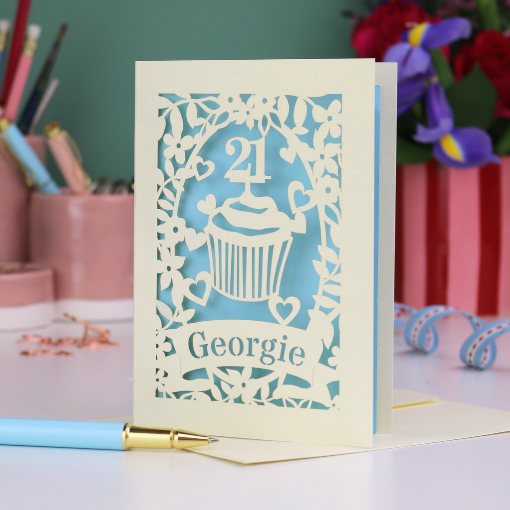 Laser-cut 21st birthday card with personalised cupcake design and 'Georgie' text on a desk with stationery items.
