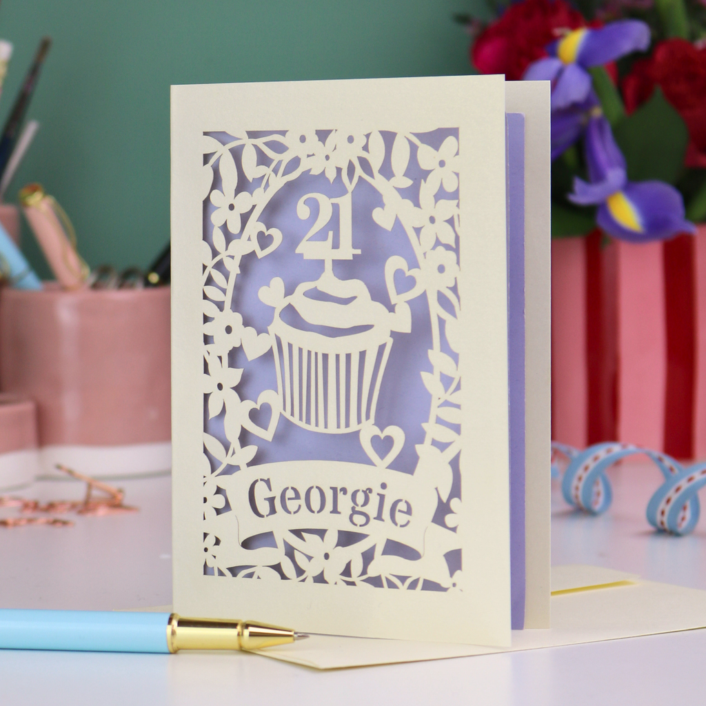 Laser-cut 21st birthday card with personalised cupcake design and 'Georgie' text on a desk with stationery items.