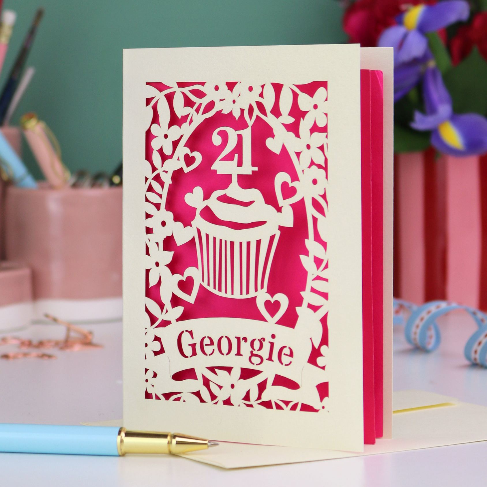 Laser-cut 21st birthday card with personalised cupcake design and 'Georgie' text on a desk with stationery items.
