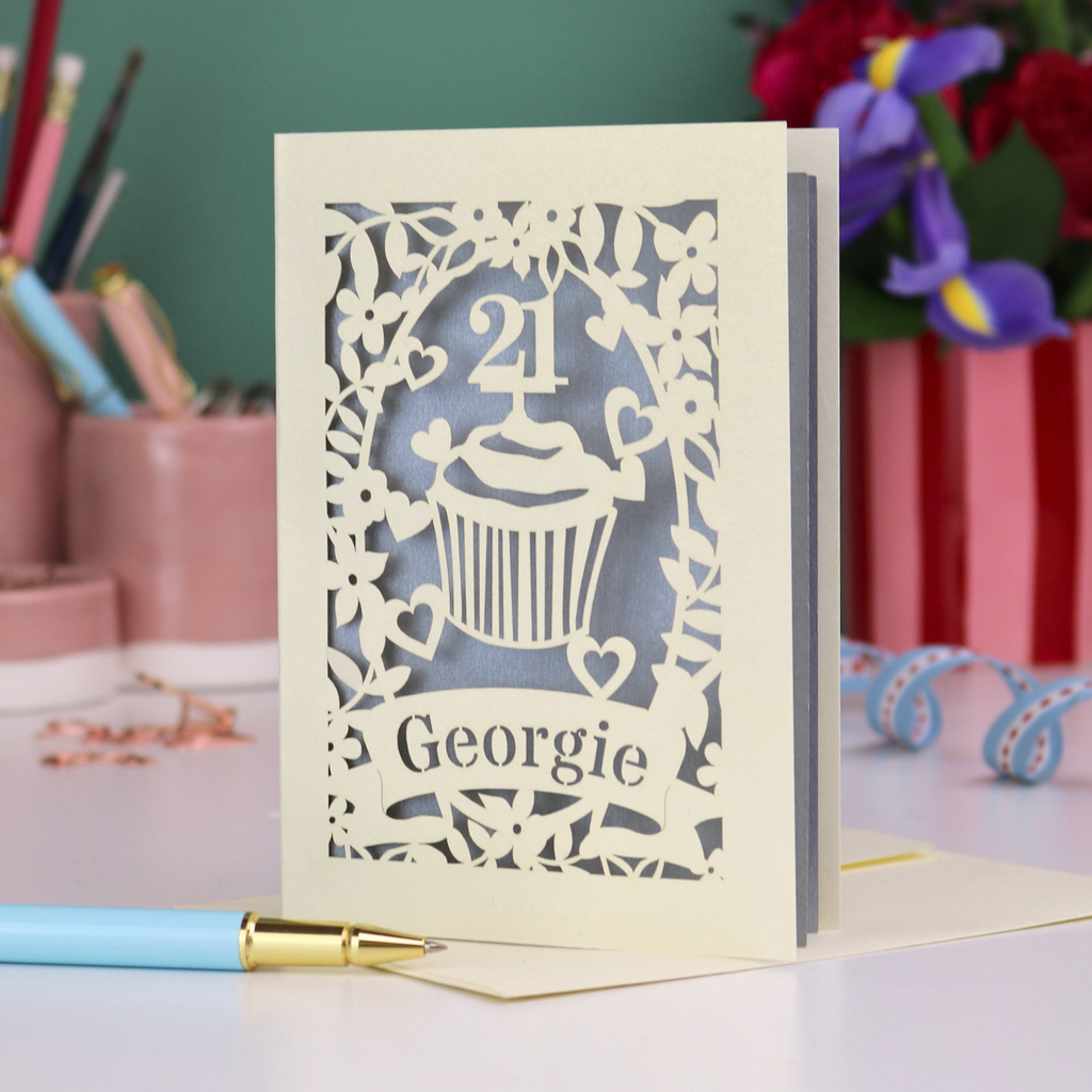 Laser-cut 21st birthday card with personalised cupcake design and 'Georgie' text on a desk with stationery items.