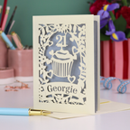 Laser-cut 21st birthday card with personalised cupcake design and 'Georgie' text on a desk with stationery items.