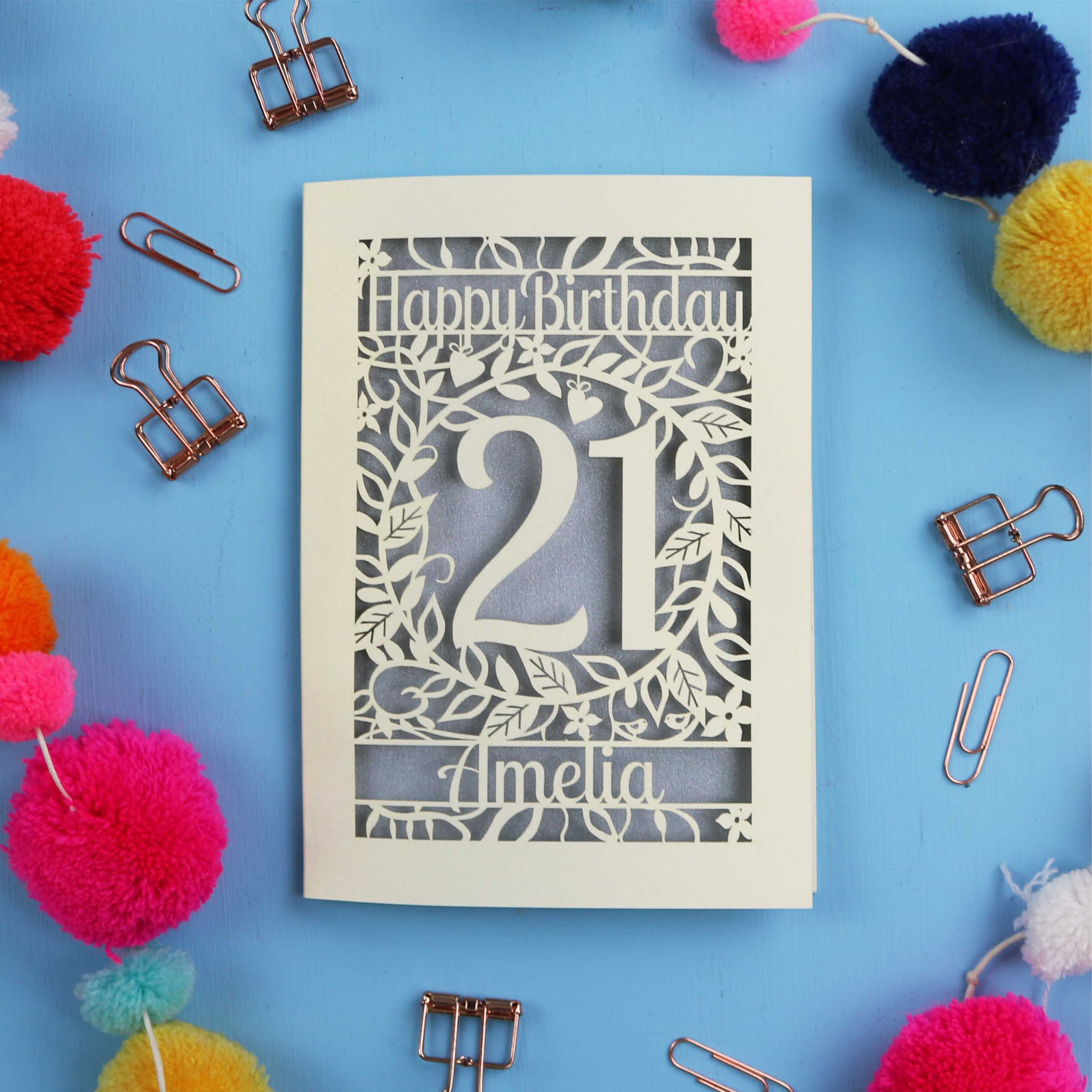 Paper Cut 21st Birthday card with 'Happy Birthday Amelia' on a blue background with colorful pom-poms and paper clips.