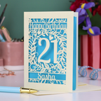 Personalised 21st Birthday card with 'Happy Birthday Sasha' and laser cut floral design on a desk with stationery items.