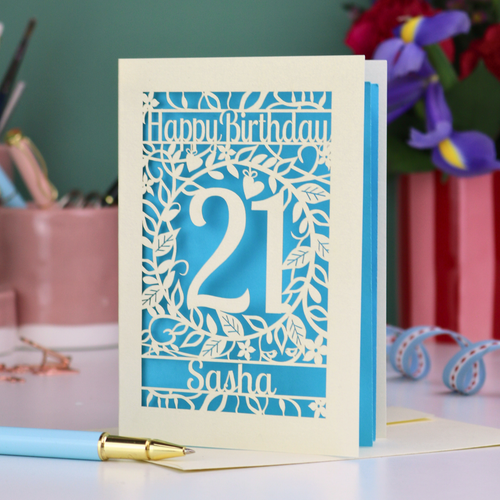 Personalised 21st Birthday card with 'Happy Birthday Sasha' and laser cut floral design on a desk with stationery items.