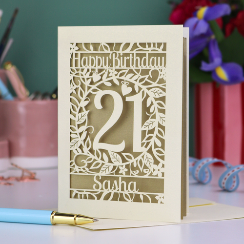 Personalised 21st Birthday card with 'Happy Birthday Sasha' and laser cut floral design on a desk with stationery items.