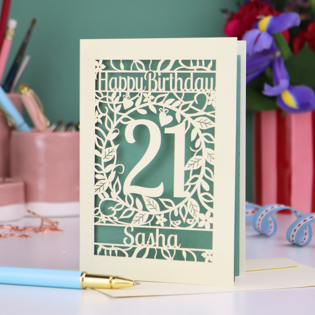 Personalised 21st Birthday card with 'Happy Birthday Sasha' and laser cut floral design on a desk with stationery items.
