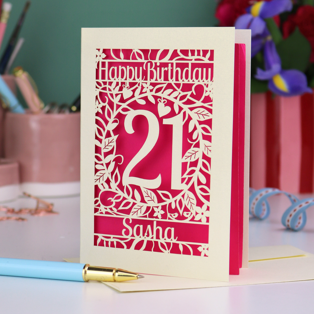 Personalised 21st Birthday card with 'Happy Birthday Sasha' and laser cut floral design on a desk with stationery items.