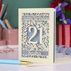 Personalised 21st Birthday card with 'Happy Birthday Sasha' and laser cut floral design on a desk with stationery items.