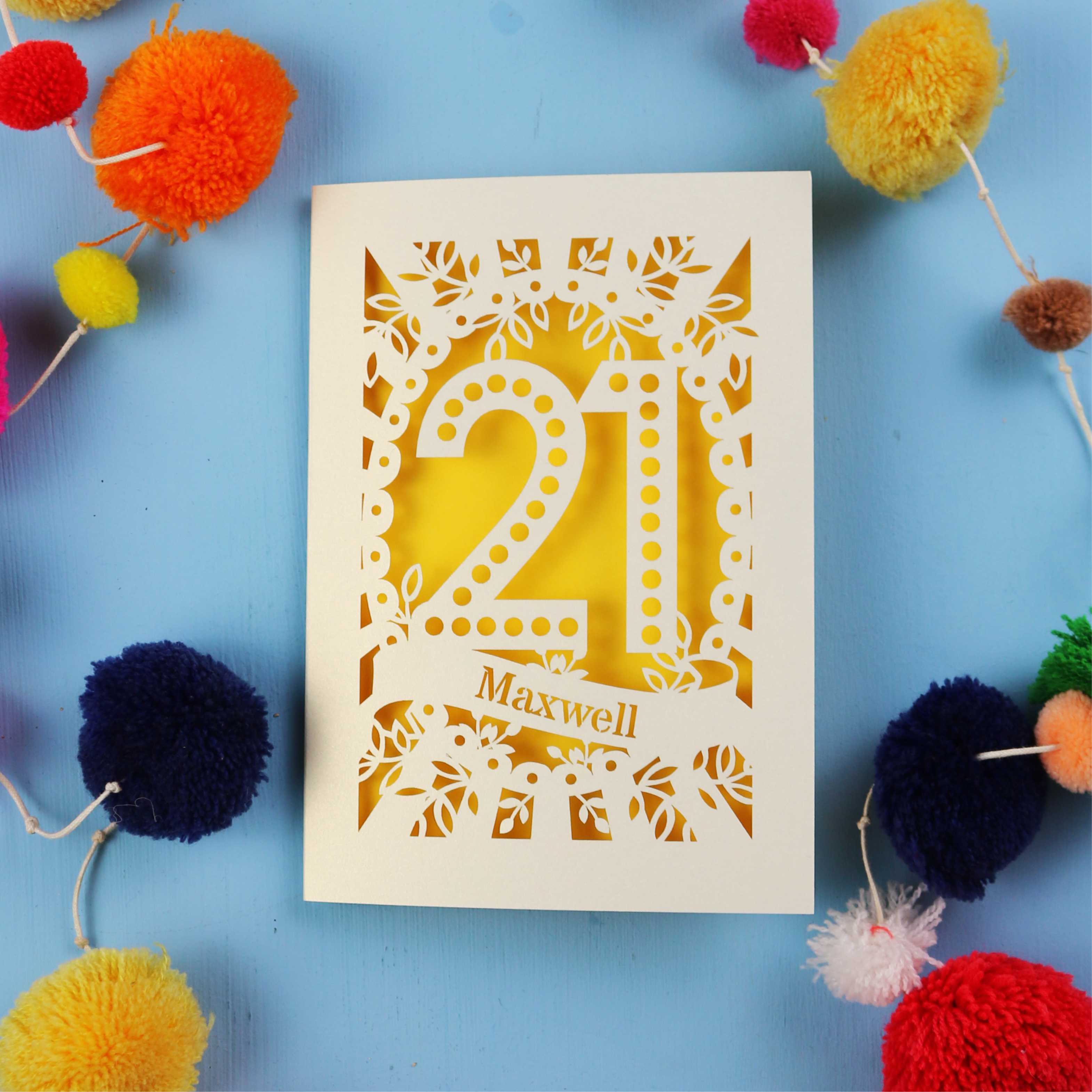 A 21st birthday Card with '21 Maxwell' design on a blue background with colourful pom-poms.
