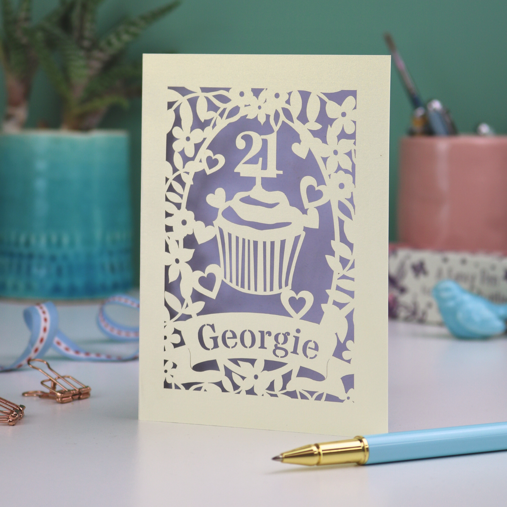 Decorative laser cut 21st birthday card with cupcake design and 'Georgie' text on a table with stationery items.