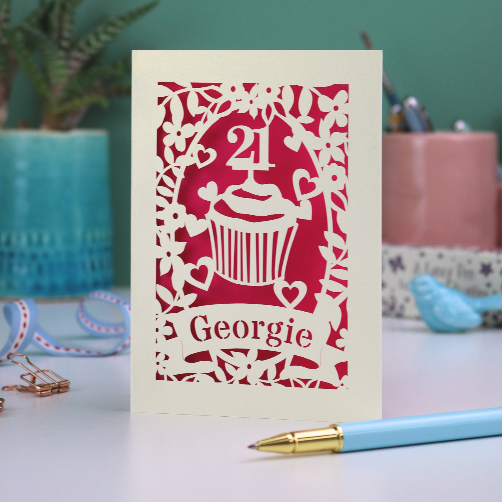 Decorative laser cut 21st birthday card with cupcake design and 'Georgie' text on a table with stationery items.