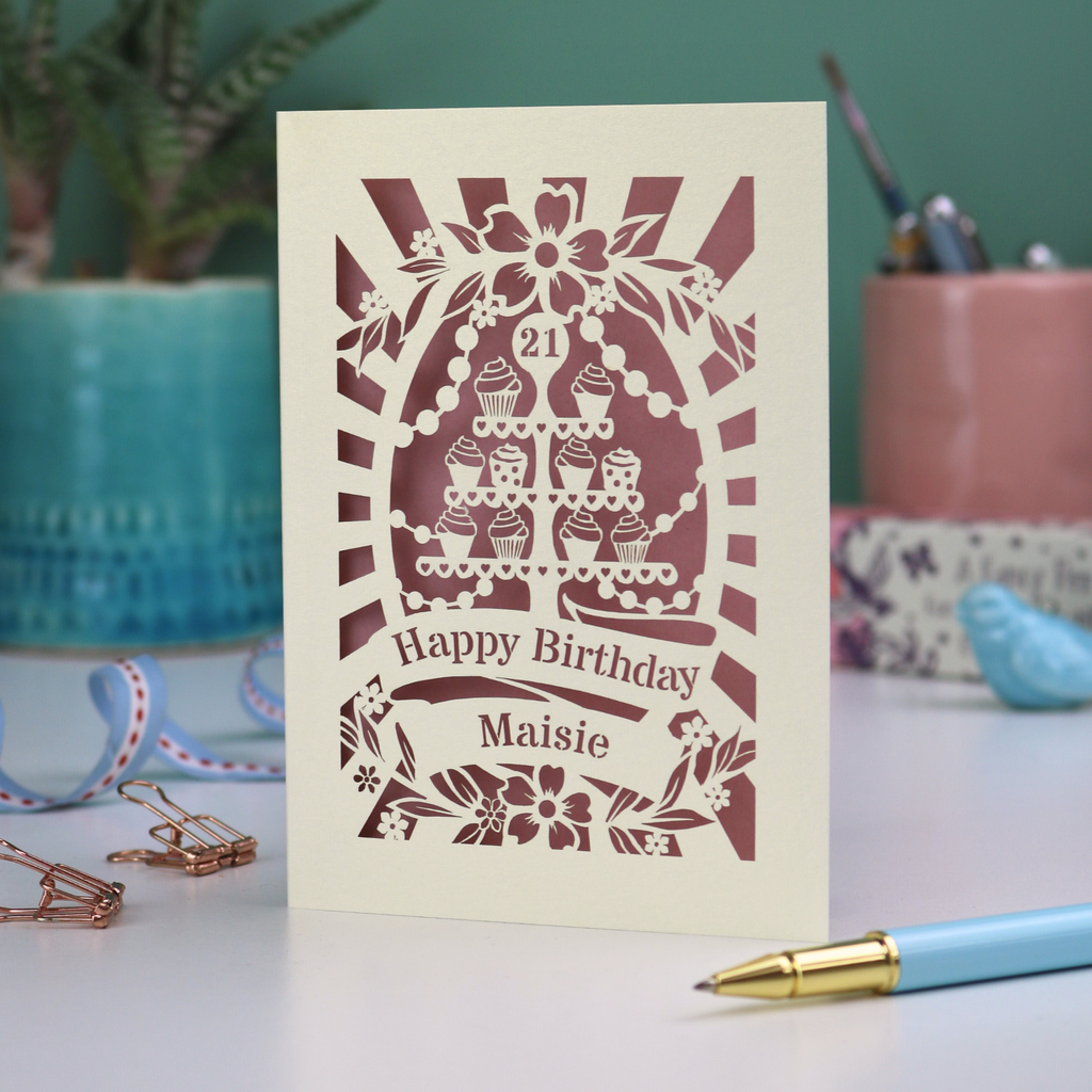 A laser cut personalised 21st Birthday card with decorative cupcake design and text on a desk with stationery items.