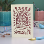 A laser cut personalised 21st Birthday card with decorative cupcake design and text on a desk with stationery items.