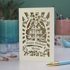 A paper cut personalised 21st Birthday card with decorative cupcake design and text on a desk with stationery items.