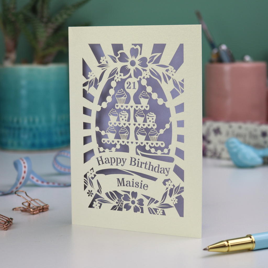 A laser cut personalised 21st Birthday card with decorative cupcake design and text on a desk with stationery items.
