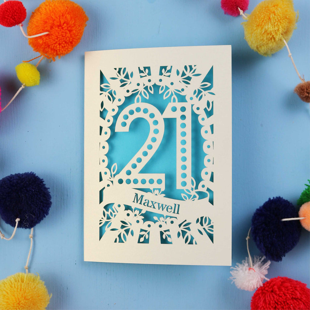 A 21st birthday Card with '21 Maxwell' design on a blue background with colourful pom-poms.