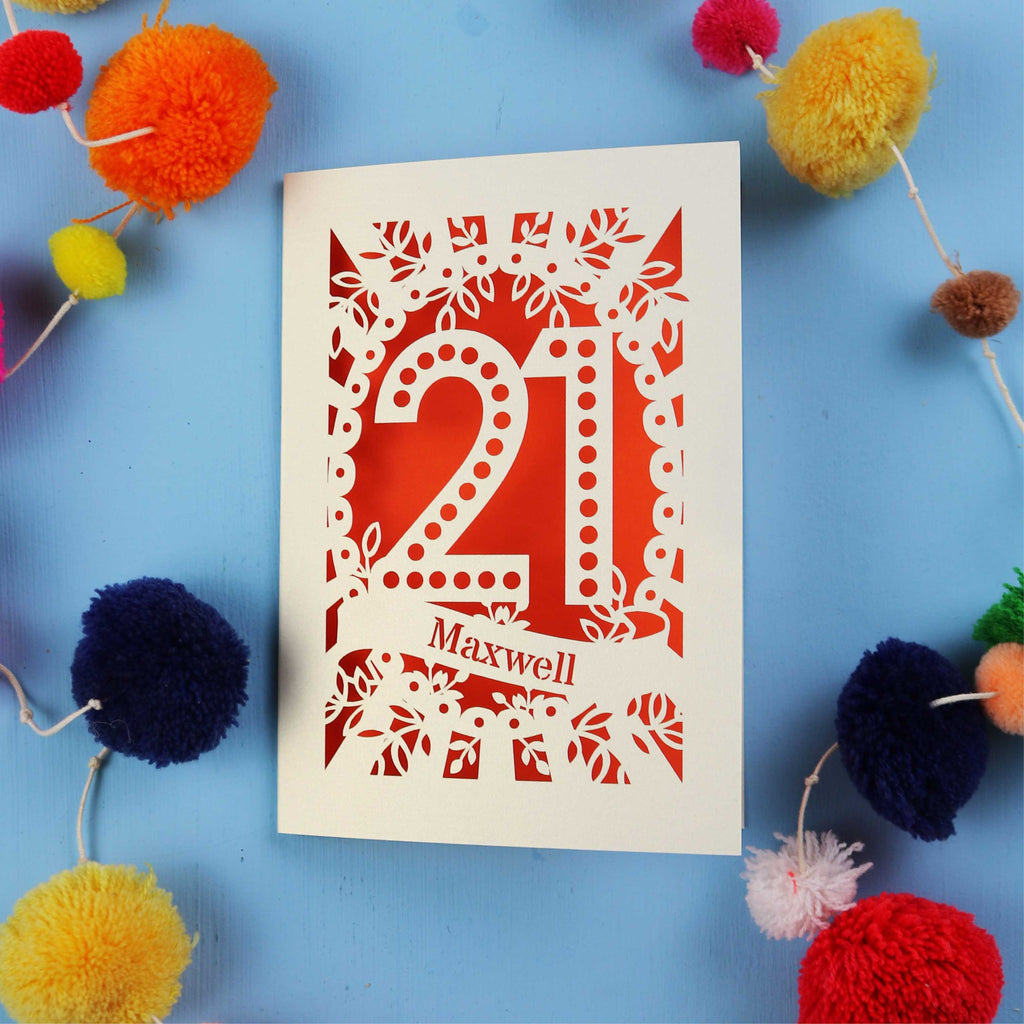 A 21st birthday Card with '21 Maxwell' design on a blue background with colourful pom-poms.
