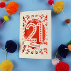 A 21st birthday Card with '21 Maxwell' design on a blue background with colourful pom-poms.