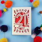 A 21st birthday Card with '21 Maxwell' design on a blue background with colourful pom-poms.