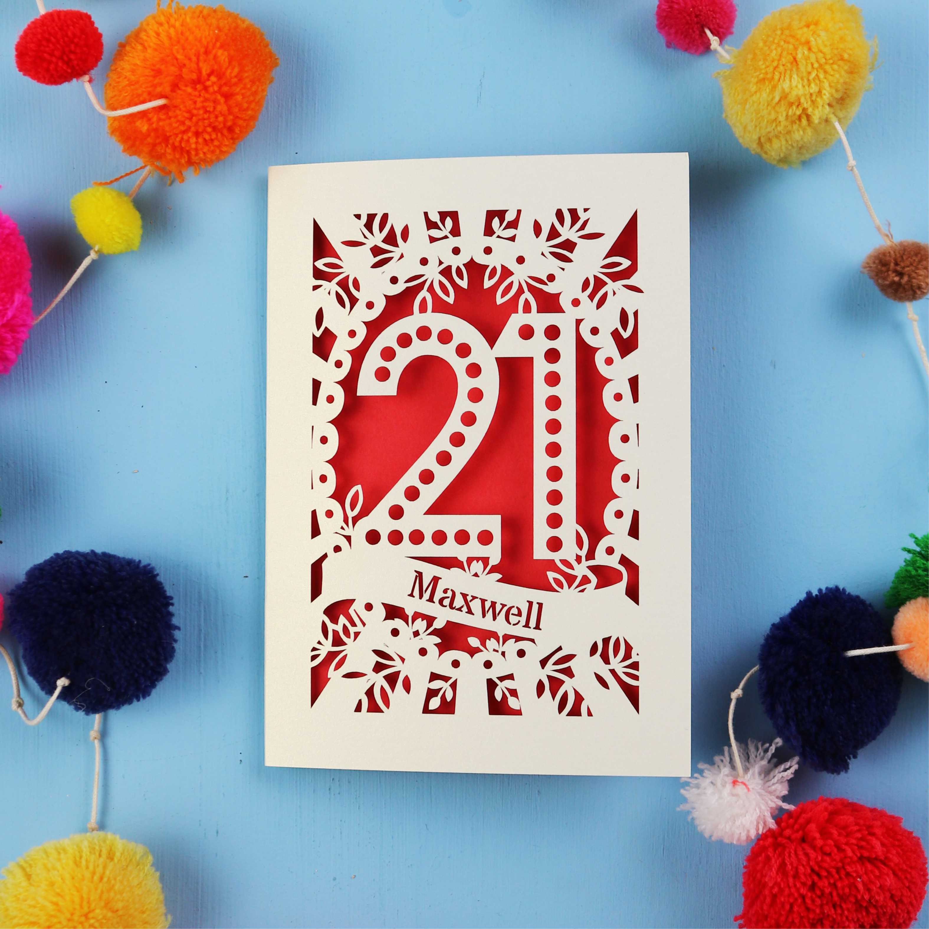 A 21st birthday Card with '21 Maxwell' design on a blue background with colourful pom-poms.