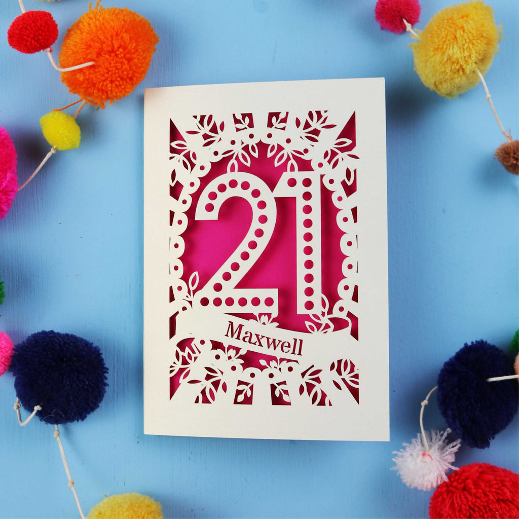 A 21st birthday Card with '21 Maxwell' design on a blue background with colourful pom-poms.