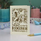 A cut out 21st birthday card, personalised with the name "Rosie", with the number 21 in the centre and woodland theme design, including tiny rabbits, a squirrel, owl, toadstools, leaves and flowers.