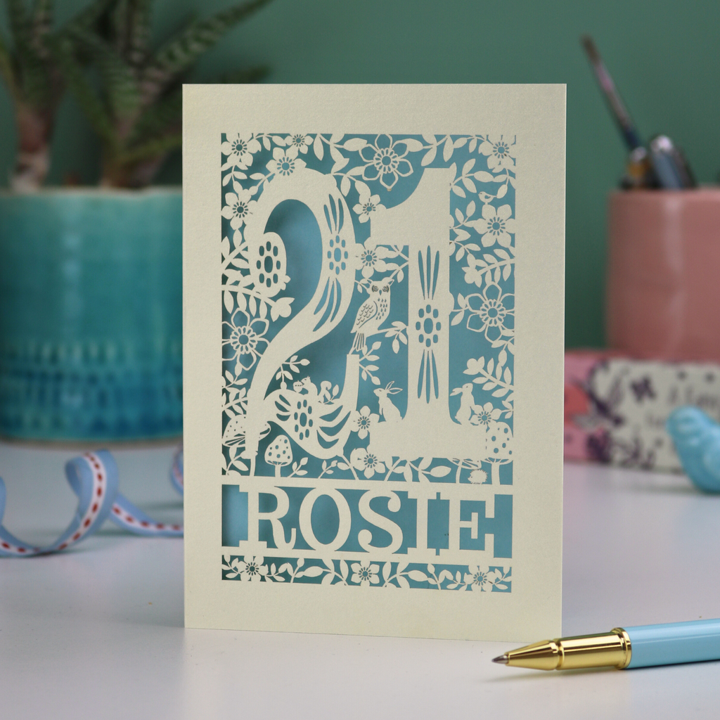 A cut out 21st birthday card, personalised with the name "Rosie", with the number 21 in the centre and woodland theme design, including tiny rabbits, a squirrel, owl, toadstools, leaves and flowers.