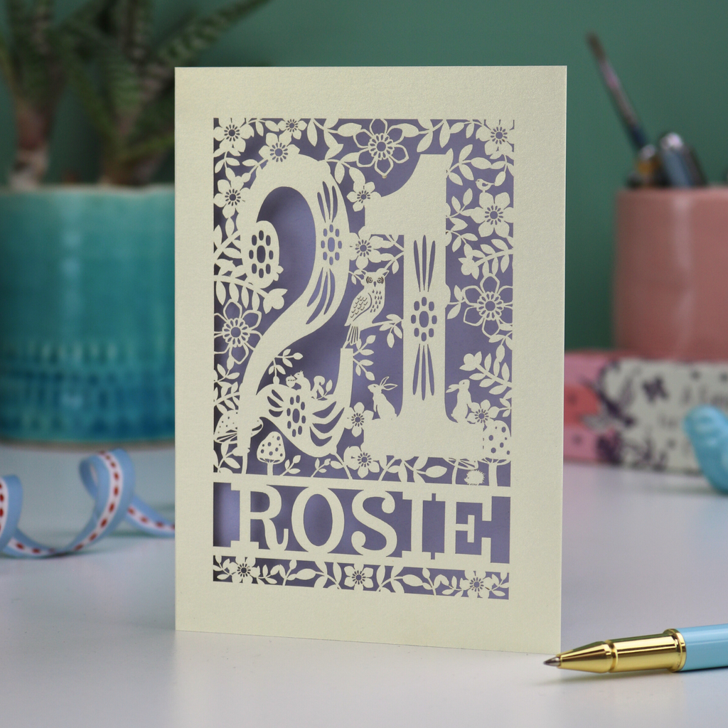 A laser cut 21st birthday card, personalised with the name "Rosie", with the number 21 in the centre and woodland theme design, including tiny rabbits, a squirrel, owl, toadstools, leaves and flowers.