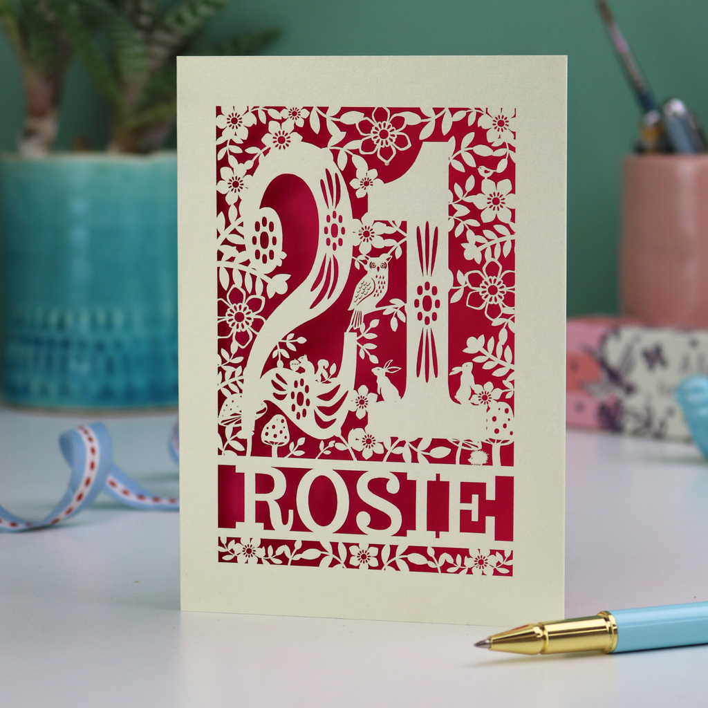 A cut out 21st birthday card, personalised with the name "Rosie", with the number 21 in the centre and woodland theme design, including tiny rabbits, a squirrel, owl, toadstools, leaves and flowers.